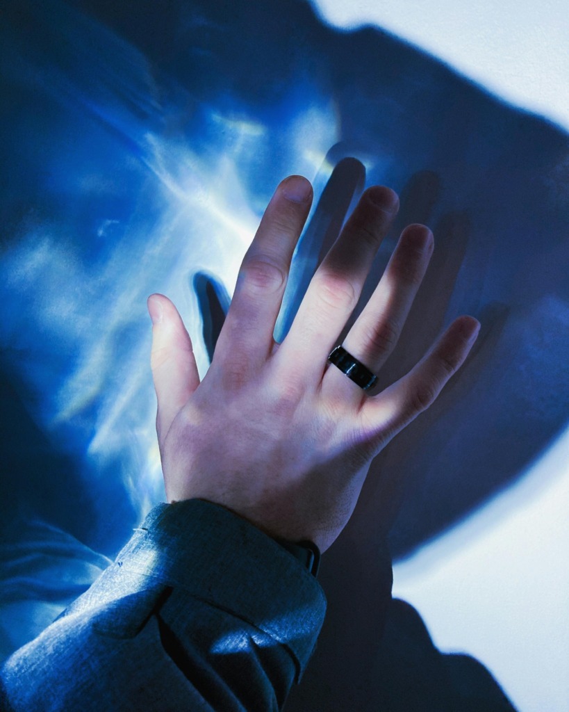 pexels-photo-11710083-11710083 A hand wearing a black ring casts a shadow on a blue abstract background.